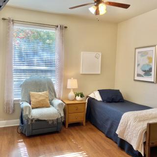 A cozy bedroom with a single bed, armchair, and soft lighting.