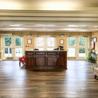 A spacious lobby area with a central reception desk, surrounded by natural light from large windows and complemented by wooden flooring and plants.