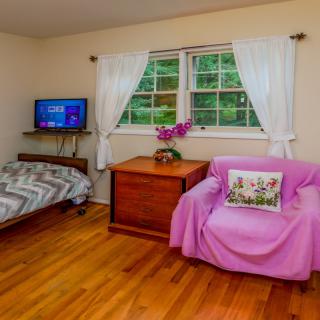 A cozy bedroom with a bed, television, and a pink-covered armchair near a window.