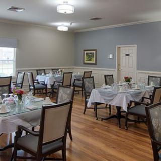 An elegantly set dining room with multiple tables and chairs, featuring a wooden floor and chandeliers.