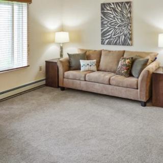 A cozy living room with a beige sofa, carpeted floor, and soft lighting from lamps.