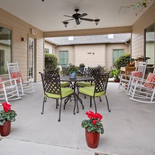 A cozy patio with rocking chairs and a table, surrounded by plants in a covered outdoor area.