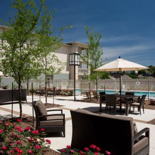 A well-maintained outdoor patio with furniture and umbrellas, surrounded by trees and landscaping.