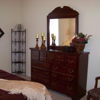 A cozy bedroom setup featuring a wooden dresser with a mirror, adorned with decorative candles and flowers.