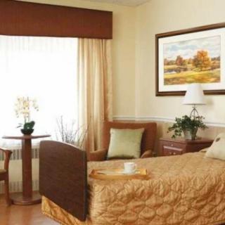 A well-decorated hospital room featuring a single bed, artwork, and a window with curtains.
