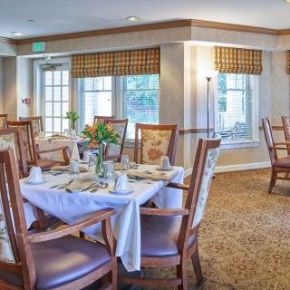 An elegantly decorated dining room with neatly arranged tables and chairs, featuring large windows and soft lighting.
