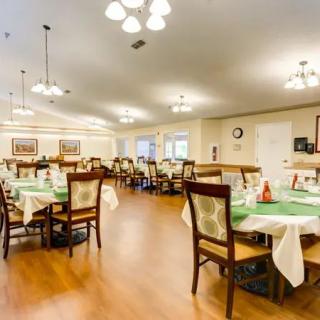 A spacious dining area with neatly arranged tables and chairs, featuring bright lighting and a wooden floor.