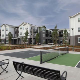 Modern apartment complex with a tennis court and outdoor seating.