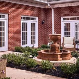 A charming courtyard with a central fountain, surrounded by a brick building and well-maintained garden spaces.