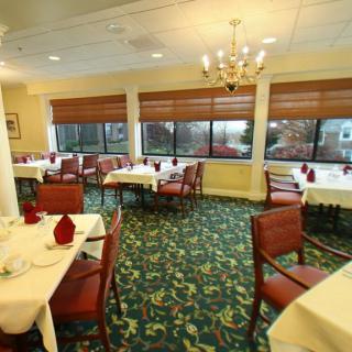 A well-lit restaurant dining area with neatly arranged tables and chairs, carpeted flooring, and large windows.