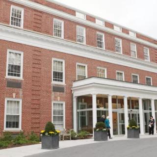 A brick building with a columned entrance and people walking by.