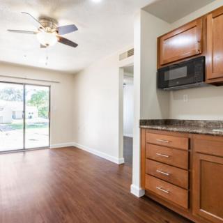 A modern kitchen space with wood flooring, featuring cabinets, a built-in microwave, ceiling fan, and a sliding glass door allowing natural light.
