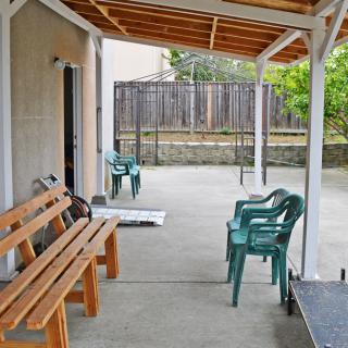 A covered patio with several plastic chairs and a wooden bench, situated in a backyard setting.