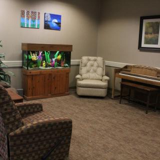 A cozy waiting room featuring a fish tank, comfortable chairs, and a piano.
