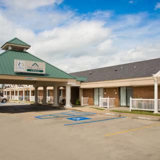 A commercial building with a covered entrance and adjacent parking lot under a cloudy sky.