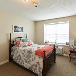 A cozy bedroom with a neatly made bed and light streaming in through the window.