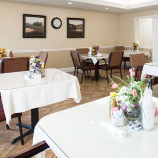 A neatly arranged dining room with several tables and chairs, decorated with flowers and framed paintings on the walls.