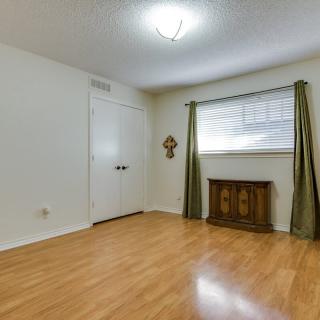 An empty room with wood flooring, green curtains, and a decorative piece under the window.