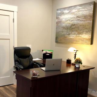 A neat and organized office space featuring a desk with a laptop, chair, lamp, and artwork on the wall.