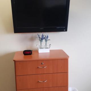 A minimalist setup with a wall-mounted TV above a wooden dresser, adorned with a small plant and decorative item.