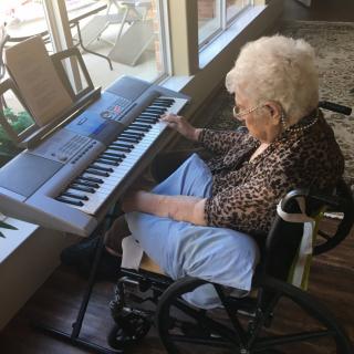 An elderly woman playing a keyboard while sitting in a wheelchair.