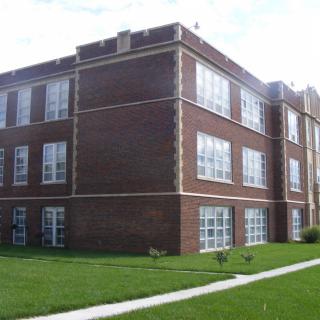 A three-story brick building with large windows and a surrounding lawn.