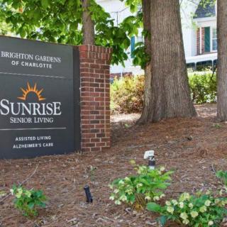 A sign for Sunrise Senior Living surrounded by trees and flowers.