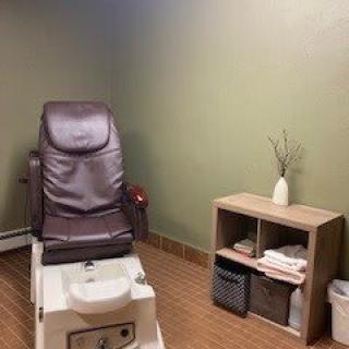 A cozy spa room featuring a pedicure chair and a small shelf with neatly arranged towels and decor.