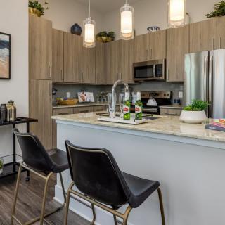 A modern kitchen featuring an island counter with stools and pendant lighting, complemented by stainless steel appliances and wood cabinets.