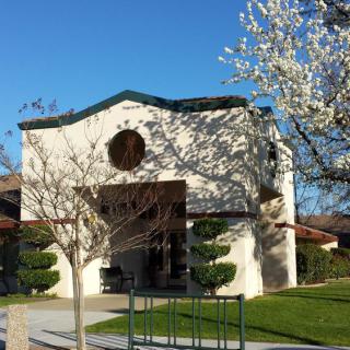 A quaint church surrounded by green lawns and blossoming trees under a clear blue sky.