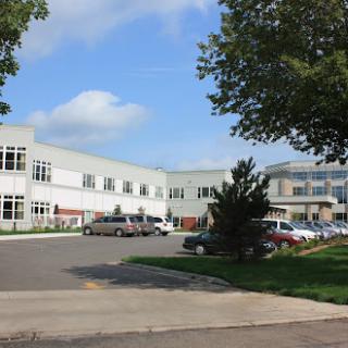 An outdoor view of a modern office building with a spacious parking lot surrounded by trees.