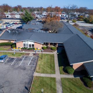 Aerial view of a suburban building with a parking lot and surrounding autumn foliage.