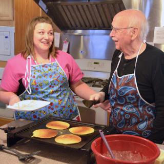 A joyful moment in the kitchen as two individuals share a laugh while making pancakes together.