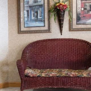 A cozy living room corner featuring a wicker sofa with a floral cushion, accompanied by framed artwork and a floral wall arrangement.