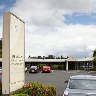 A hotel entrance with a parking lot and several cars under a cloudy sky.