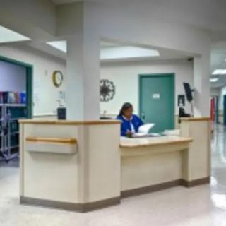 Interior of a hospital reception area with a nurse attending paperwork at the station.