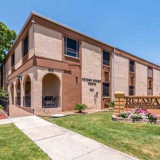 A two-story brick apartment building with landscaped surroundings and a paved sidewalk.