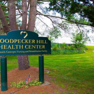 A sign for Woodpecker Hill Health Center surrounded by trees and greenery.