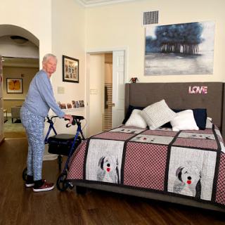 An elderly person using a walker in a cozy bedroom setting.