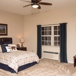 A cozy bedroom with a plaid bedspread, carpeted floor, and a ceiling fan.