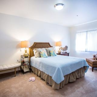 A cozy bedroom with a neatly made bed, bedside lamps, and a window letting in natural light.