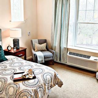 A cozy and well-lit bedroom with a patterned bedspread, armchair, and large window.