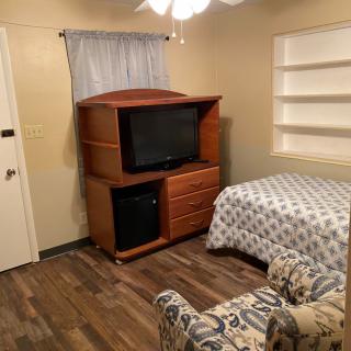 A cozy bedroom with a television, bed, and armchair.