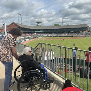 An elderly person in a wheelchair enjoying a baseball game with a companion at the stadium.