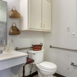 A neatly organized bathroom with a toilet, sink, and cabinets featuring safety grab bars.