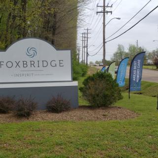 The Foxbridge entrance sign is situated along a roadside with greenery and promotional flags.