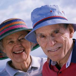 An elderly couple smiling outdoors, enjoying a sunny day while wearing colorful hats.