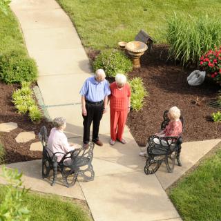 A group of seniors enjoying a conversation outdoors in a garden setting.