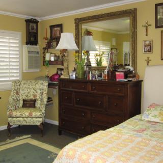 A cozy bedroom featuring a dresser with a large mirror, surrounded by decorative elements and a floral armchair.