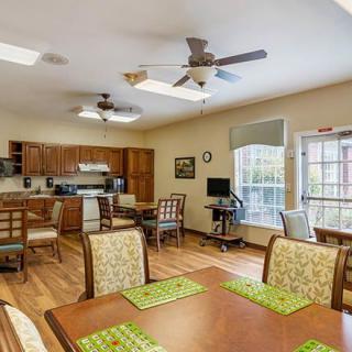 A cozy dining area and kitchen space featuring wooden furniture and flooring, with ceiling fans and ample natural light from large windows.